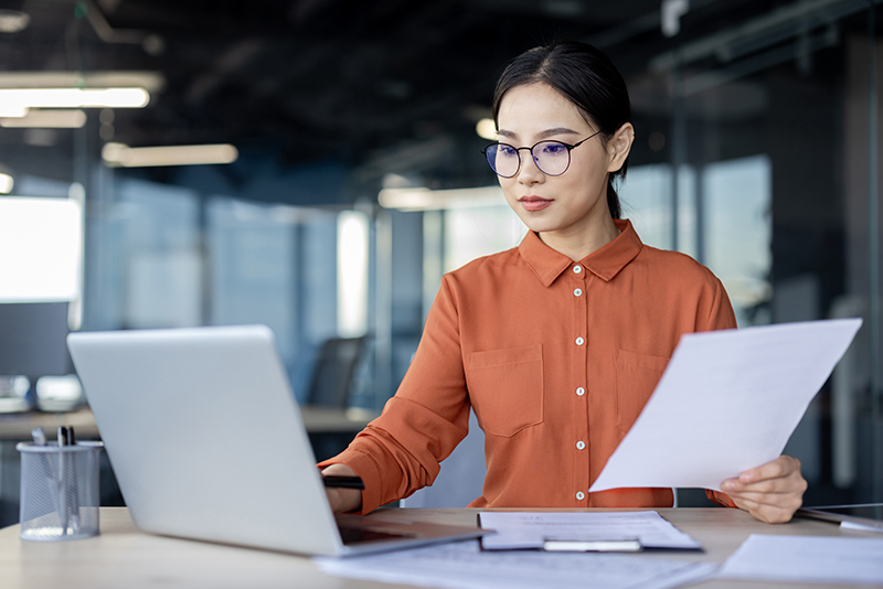 Asian,Financial,Woman,Working,Inside,Office,With,Documents,,Papers,Behind